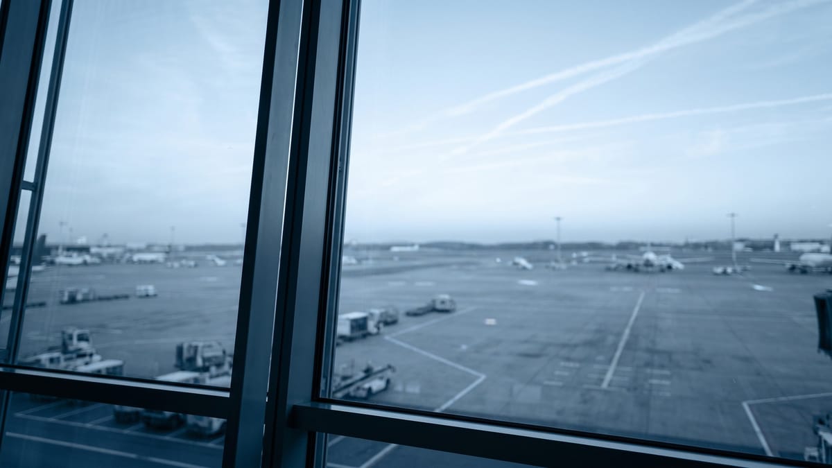 Piazzale aeroportuale visto in lontananza da una grande vetrata, cielo azzurro con scie